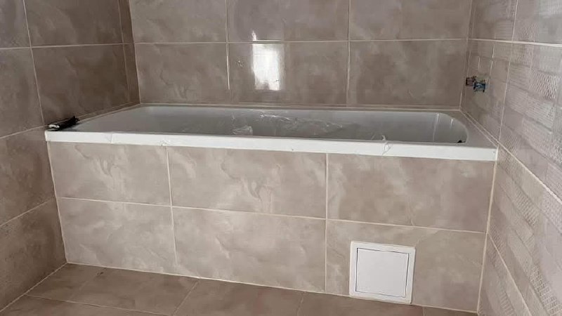 A beburkolt kád a márványhatású csempével, a kád burkolatában fehér szervizajtó