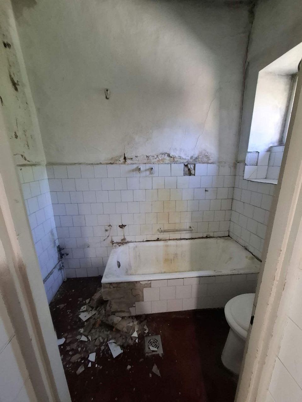 A régi fürdőszoba bontás közben: régi kád, fehér csempe, a padlón törmelék
