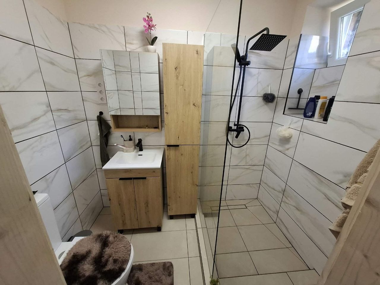 Az elkészült fürdőszoba: üvegfalas zuhanyzó, márványhatású csempe, mosdószekrény