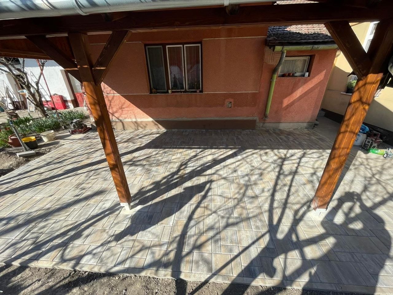 A térkövezett terasz a fa tartóoszlopokkal, a háttérben a ház